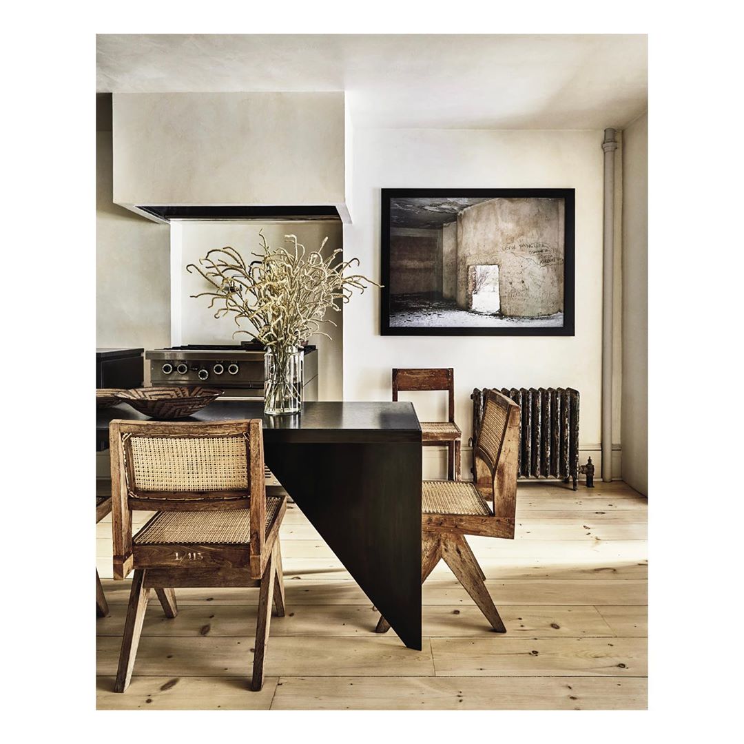 Dining room with a black table surrounded by cane chairs, featuring a vase of dried floral arrangement and an art print on the wall.