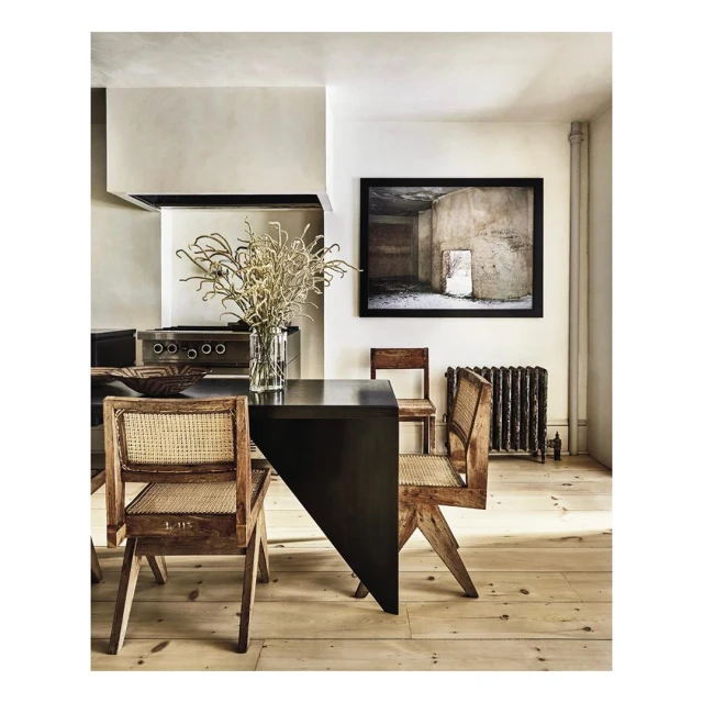 Dining room with a black table surrounded by cane chairs, featuring a vase of dried floral arrangement and an art print on the wall.