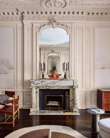 Ornate interior featuring a marble fireplace with a bust, flanked by candelabras and a mirror in a room with decorative moulding.