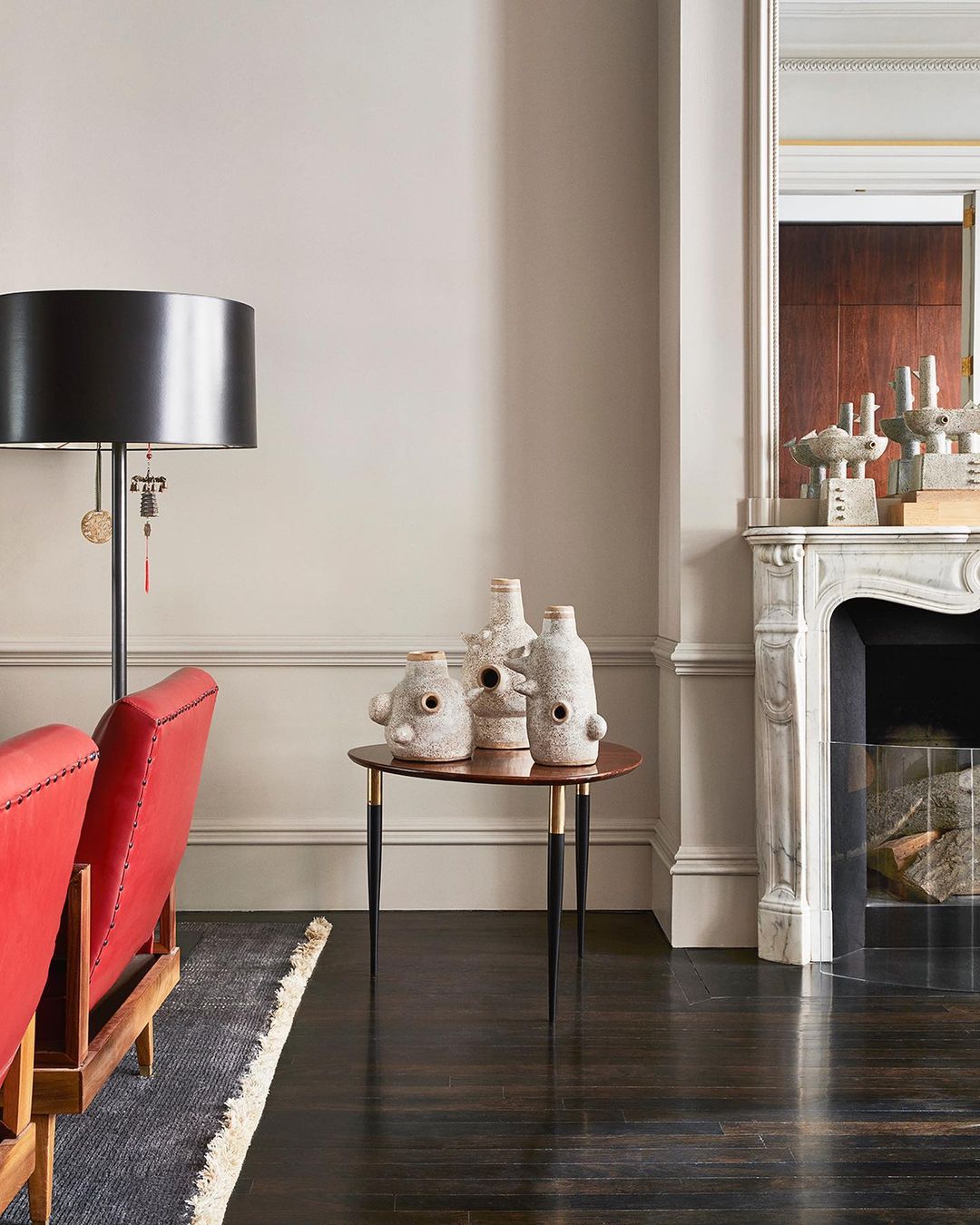 Living room interior featuring a red mid-century modern chair, a round side table holding vases, fireplace, and a black floor lamp.