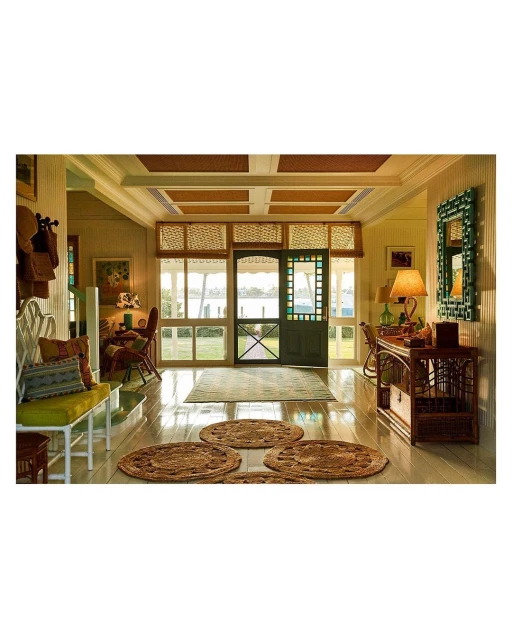 Brightly lit hallway with wicker furniture, round rugs, white trim, and a screened door leading to an outdoor view of water and trees.