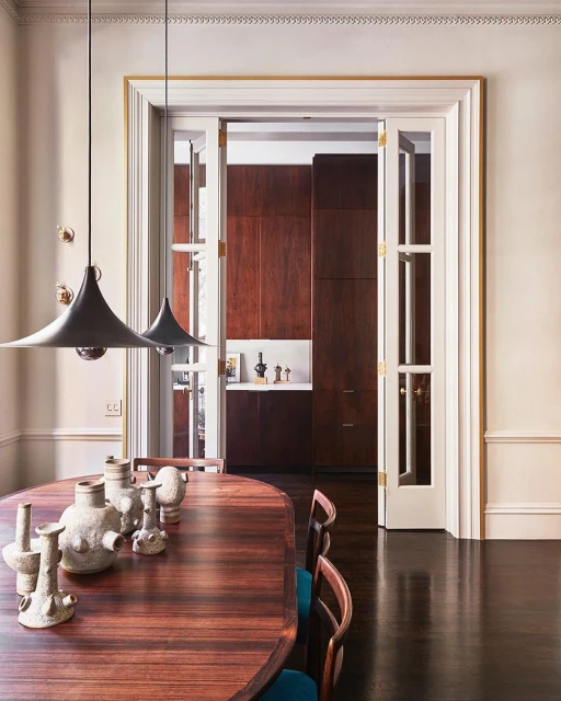 Contemporary dining room featuring a wood table with decorative vases, pendant lights, and an open doorway leading to another room.