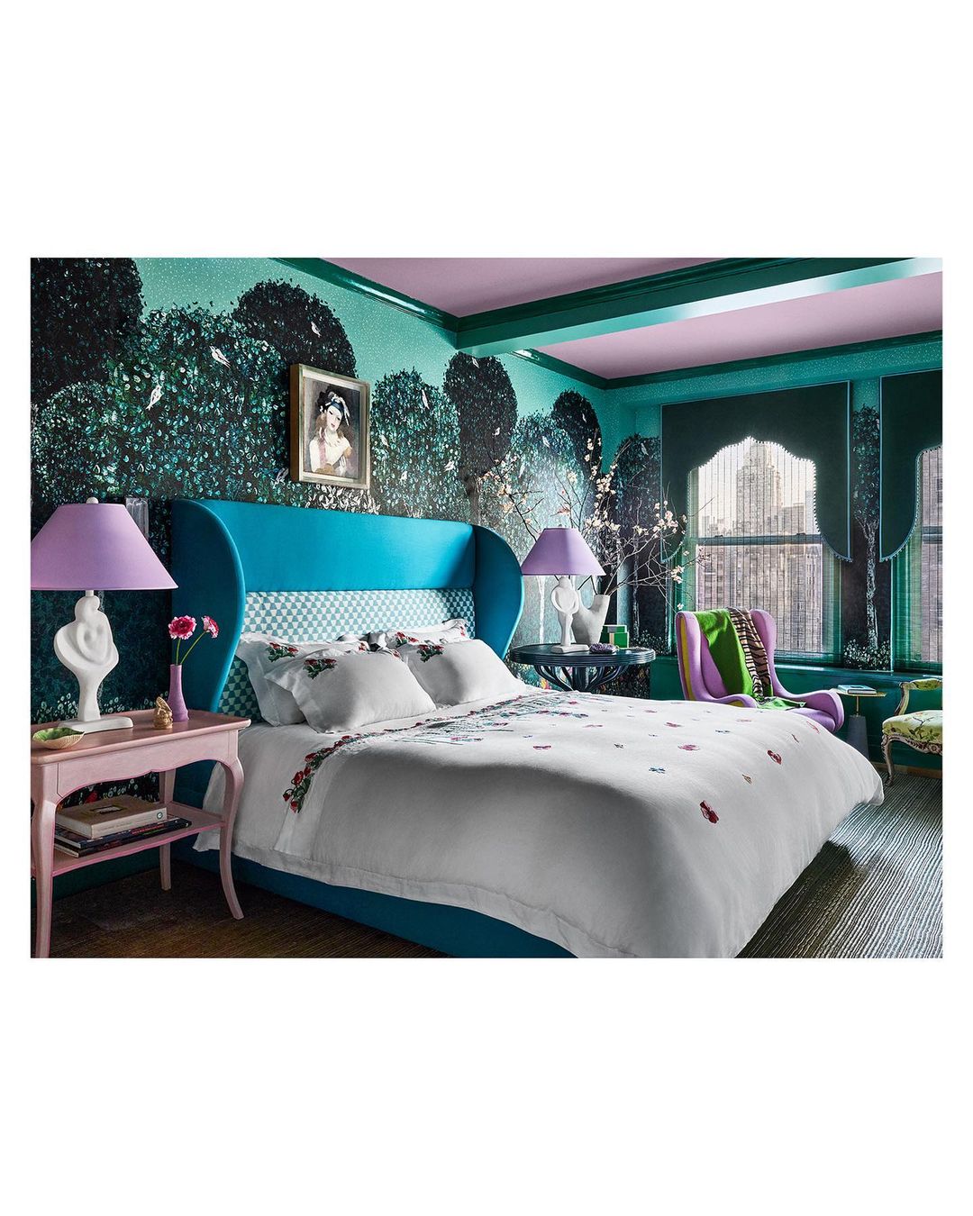 Interior bedroom design featuring a large bed with floral bedding, turquoise headboard, floral wallpaper, and a pink bedside table with a lamp.