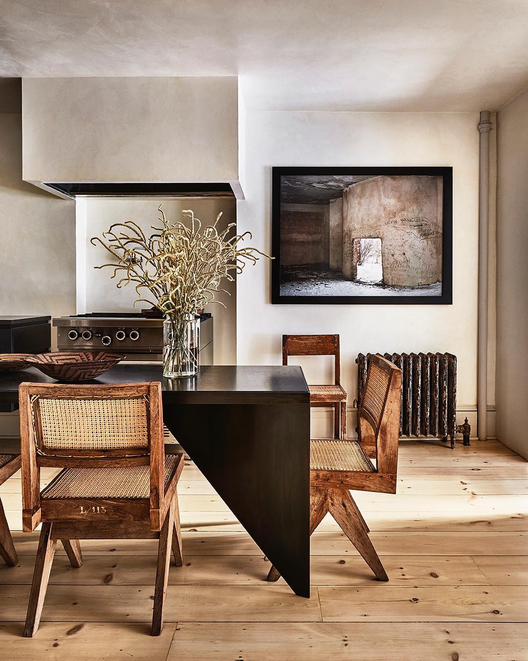 Indoor shot of a dining area with a black table, four chairs, and a framed architectural photograph on a cream-colored wall.