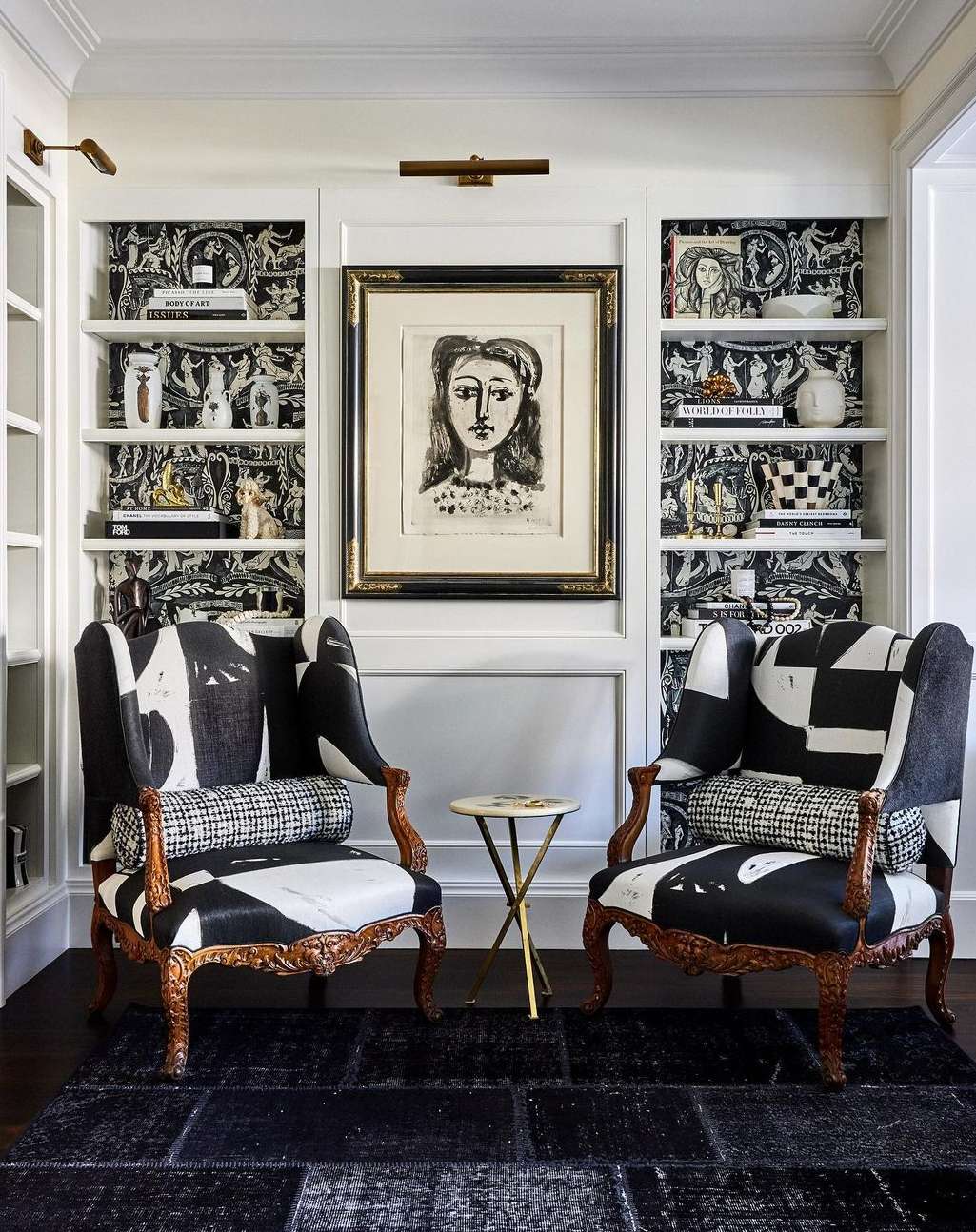 Interior design with two black-and-white patterned armchairs, a side table, and a wall unit with shelves and artwork in a home setting.