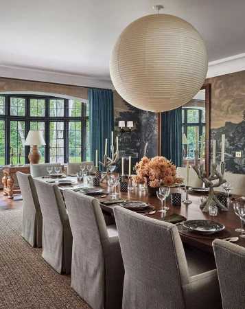 Formal dining room interior with a long wood table set with plates and glassware, surrounded by upholstered chairs, and natural light.