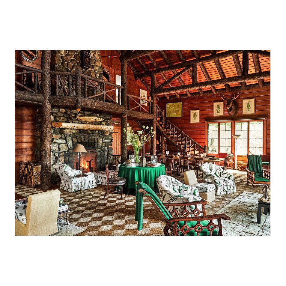 Cozy living room featuring a stone fireplace, wood paneling, and patterned armchairs, creating a warm, inviting, rustic lodge atmosphere.