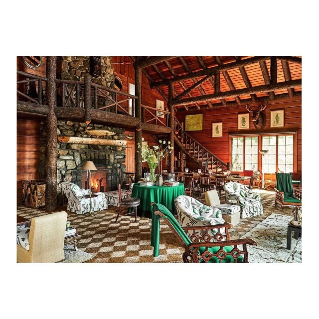 Cozy living room featuring a stone fireplace, wood paneling, and patterned armchairs, creating a warm, inviting, rustic lodge atmosphere.