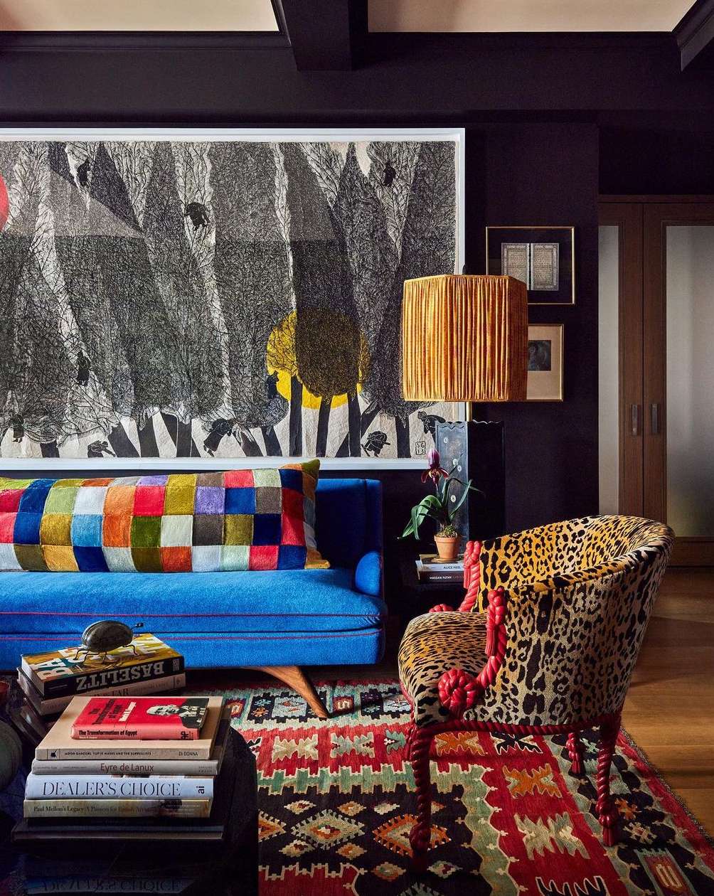 Eclectic living room interior with a bright blue sofa, leopard print armchair, patterned rug, and large abstract art on dark walls.