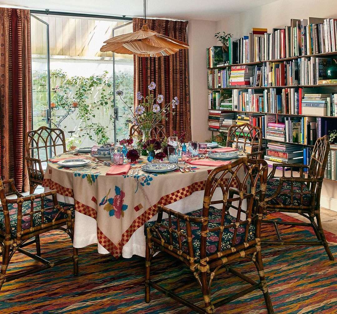 Indoor dining area with a floral tablecloth, bamboo chairs, and bookshelf filled with books, creating a cozy and inviting atmosphere.
