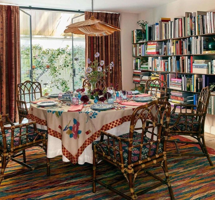Indoor dining area with a floral tablecloth, bamboo chairs, and bookshelf filled with books, creating a cozy and inviting atmosphere.