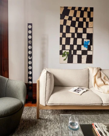 Living room interior featuring a beige sofa, modern art piece, gray chair, standing decorative lamp, and patterned gray rug.