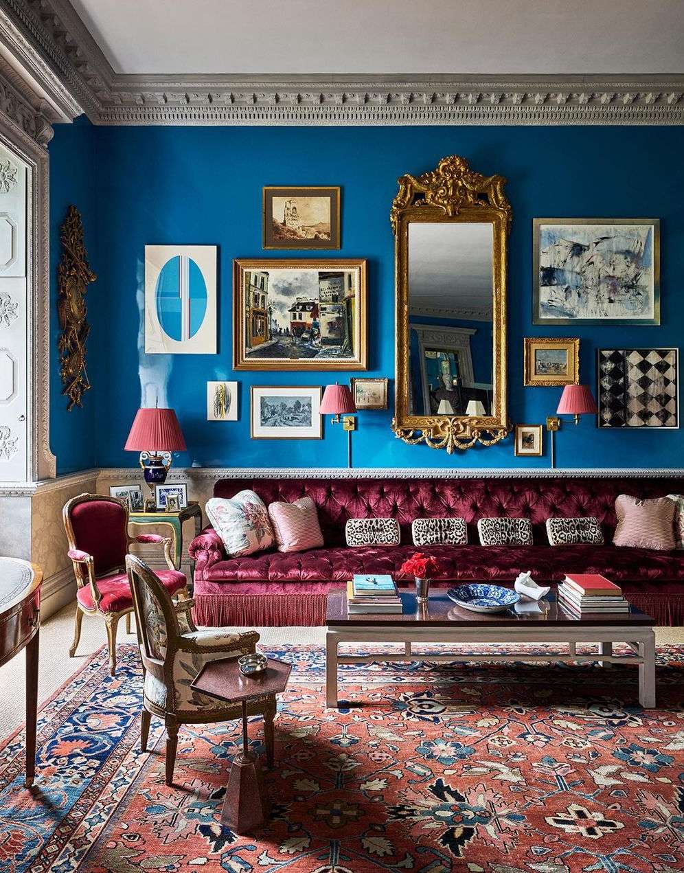 Ornate living room interior with velvet sofa, patterned rug, antique chairs, paintings, mirror, lamps against teal walls; a luxury aesthetic.