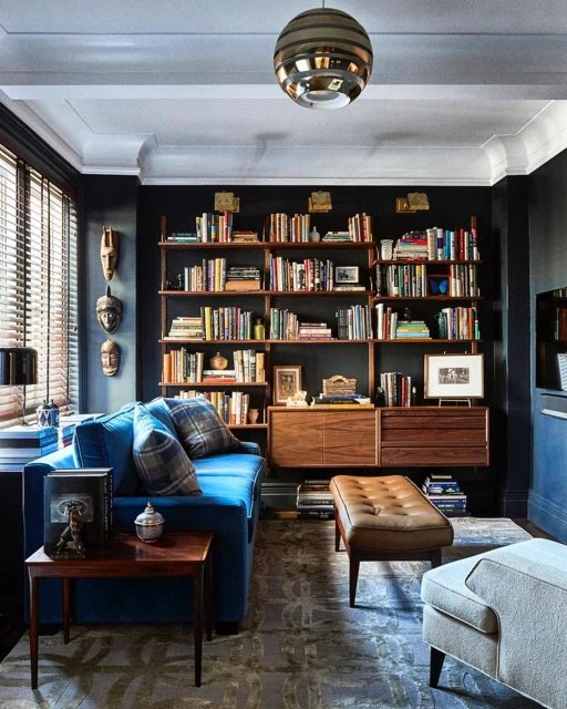 Cozy living room interior with blue sofa, wooden bookshelf filled with books, area rug, and decorative objects in a home.