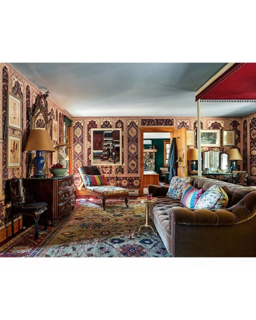Ornate living room interior with brown velvet couch, patterned wallpaper, area rug, wooden cabinet, and eclectic decor.