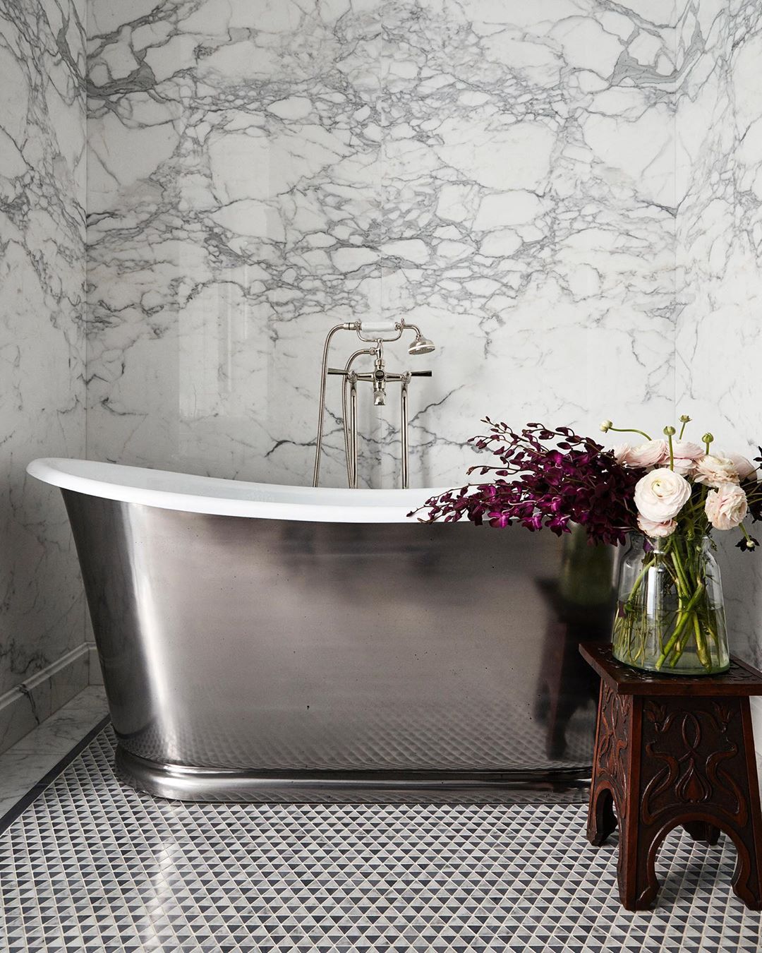 Chrome bathtub in a marble-clad bathroom with flowers. Interior design featuring a modern bathroom with luxury materials and decorations.
