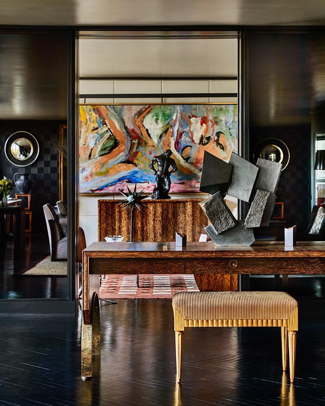 Living room interior with abstract art and decorative objects in black and gold, with hardwood floors, lighting, and accent furniture.