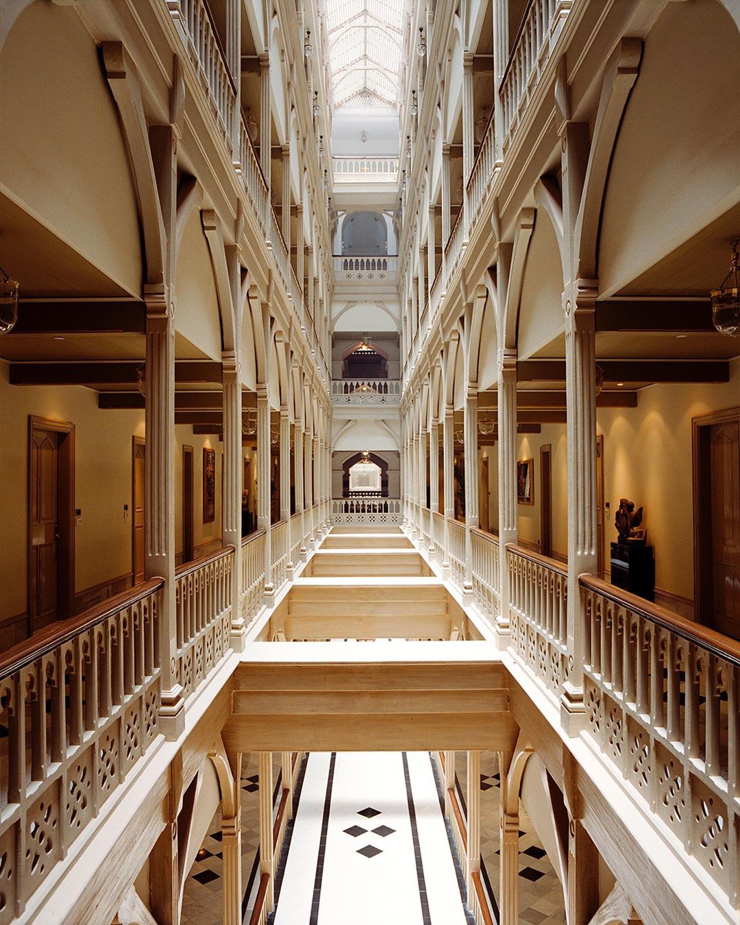 Interior architecture showing multiple floors and arched columns of an indoor hallway with decorative railings and a skylight above.