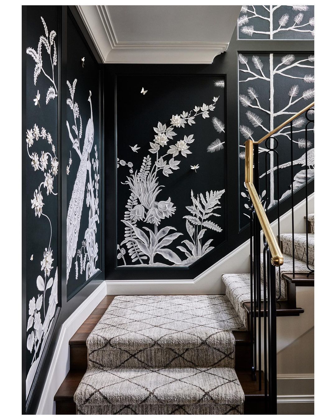 Interior view of a staircase with patterned carpet, black handrail, and walls adorned with white floral and bird illustrations.