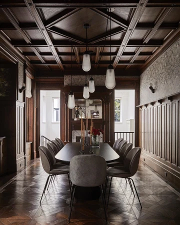 Interior of a formal dining room featuring a long dark wooden table surrounded by grey chairs, with pendant lights overhead.