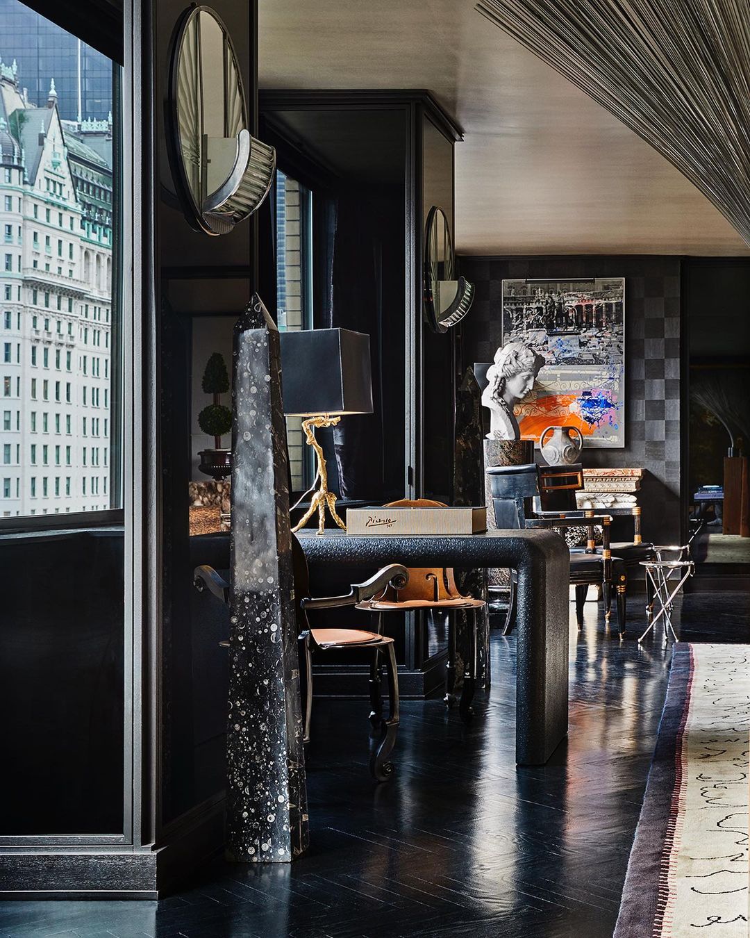 Elegant interior featuring modern furnishings, a textured desk, and a view of a city skyline through a large window.