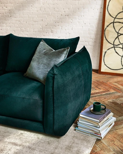 Living room interior featuring a dark green velvet sofa with a throw pillow, a stack of books, and decorative art, indoors.