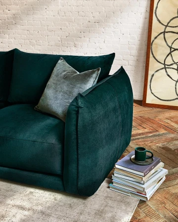 Living room interior featuring a dark green velvet sofa with a throw pillow, a stack of books, and decorative art, indoors.