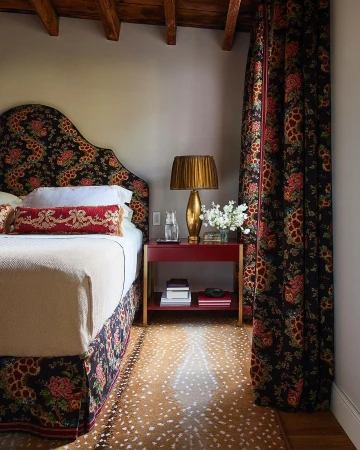 Bedroom interior with a bed featuring a floral headboard and bedding, alongside a red bedside table with a lamp and decor.