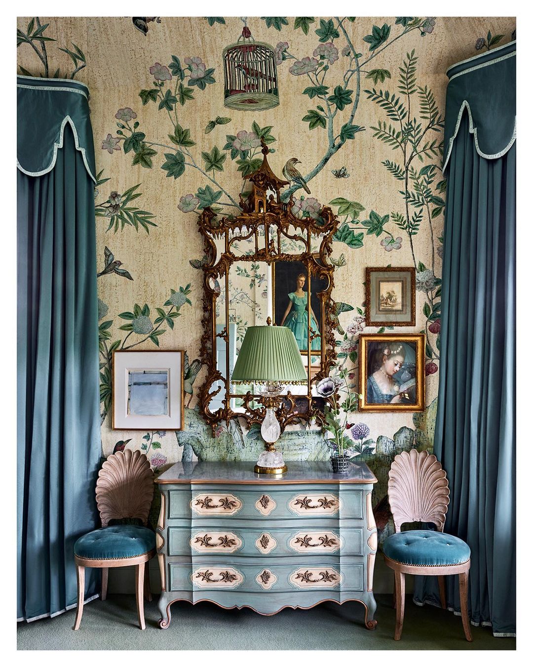 Interior design with antique chest of drawers, ornate mirror, floral wallpaper, two chairs, and teal drapery framing the scene.