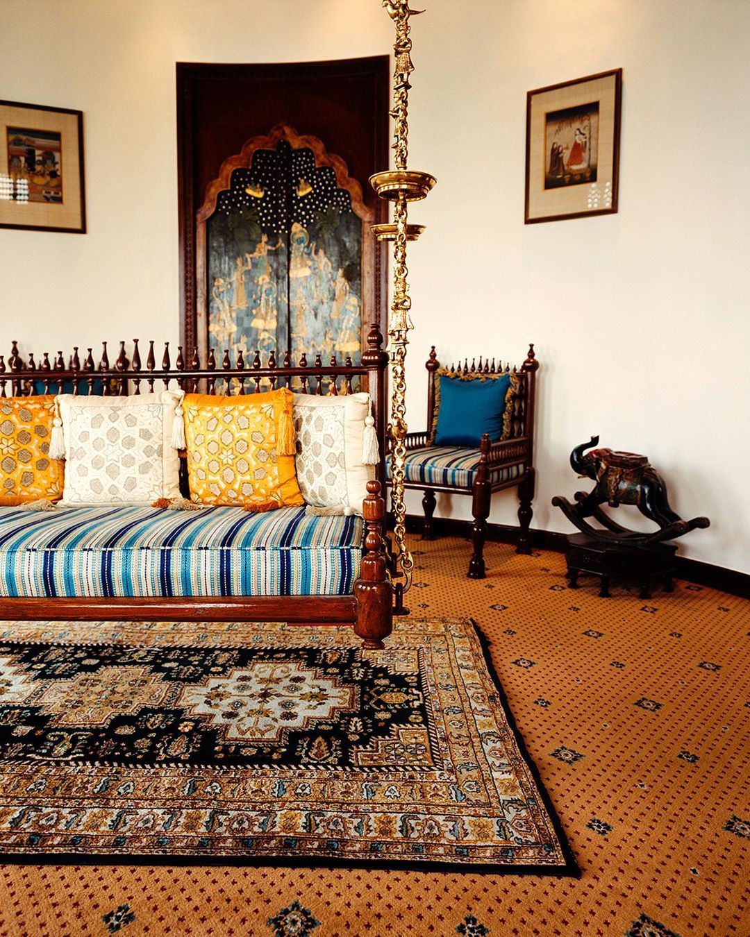 Traditional Indian-style interior featuring a bed swing with colorful pillows, ornate rug, wooden chair, and artwork on the walls.