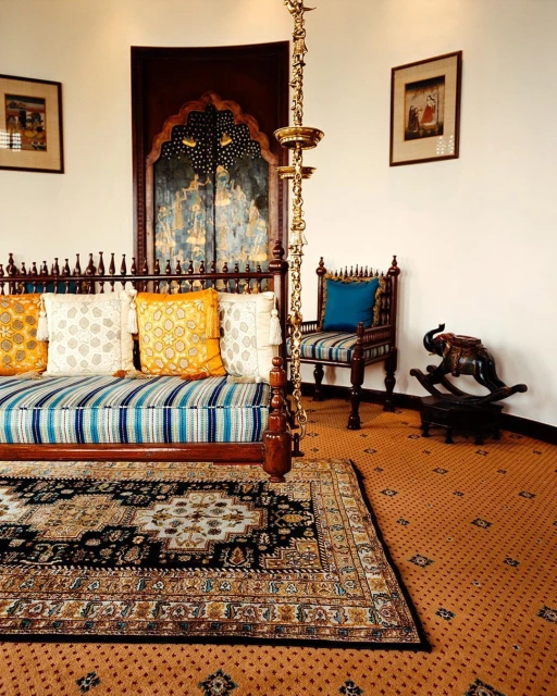 Traditional Indian-style interior featuring a bed swing with colorful pillows, ornate rug, wooden chair, and artwork on the walls.