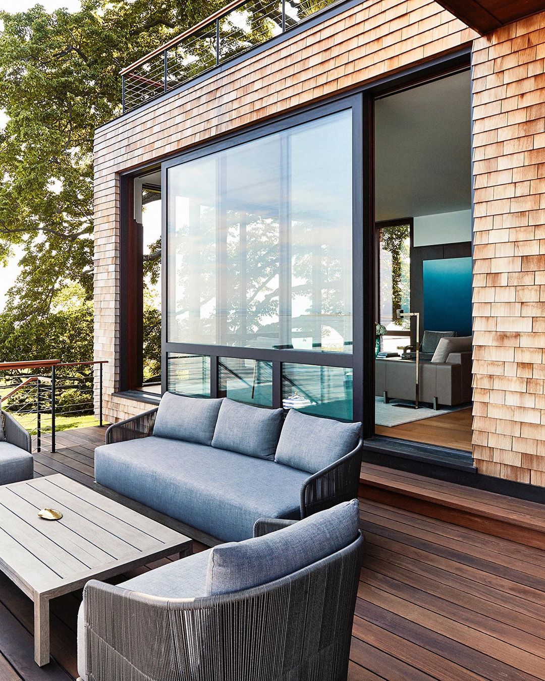 Exterior view of a modern home with a wooden deck, outdoor furniture, large sliding glass doors, and wood shingle siding.