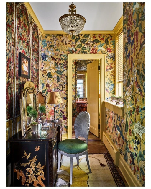 Ornate interior hallway with floral wallpaper, antique furniture, chandelier, and an open doorway leading to another room.