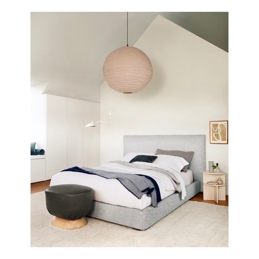 Bedroom interior with a light gray platform bed, round paper lantern pendant, and a gray round ottoman on a shag rug.
