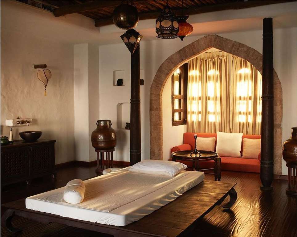 Day spa setup indoors with a massage table, seating area, decorative lanterns, and arched window with natural light.