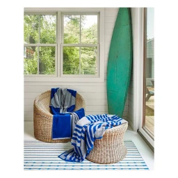 Wicker chair and stool draped with blue and grey striped blankets next to a turquoise surfboard indoors