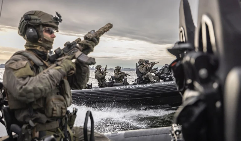 A group of armed special forces in tactical gear riding on a black boat in the water, armed with rifles, ready for action.