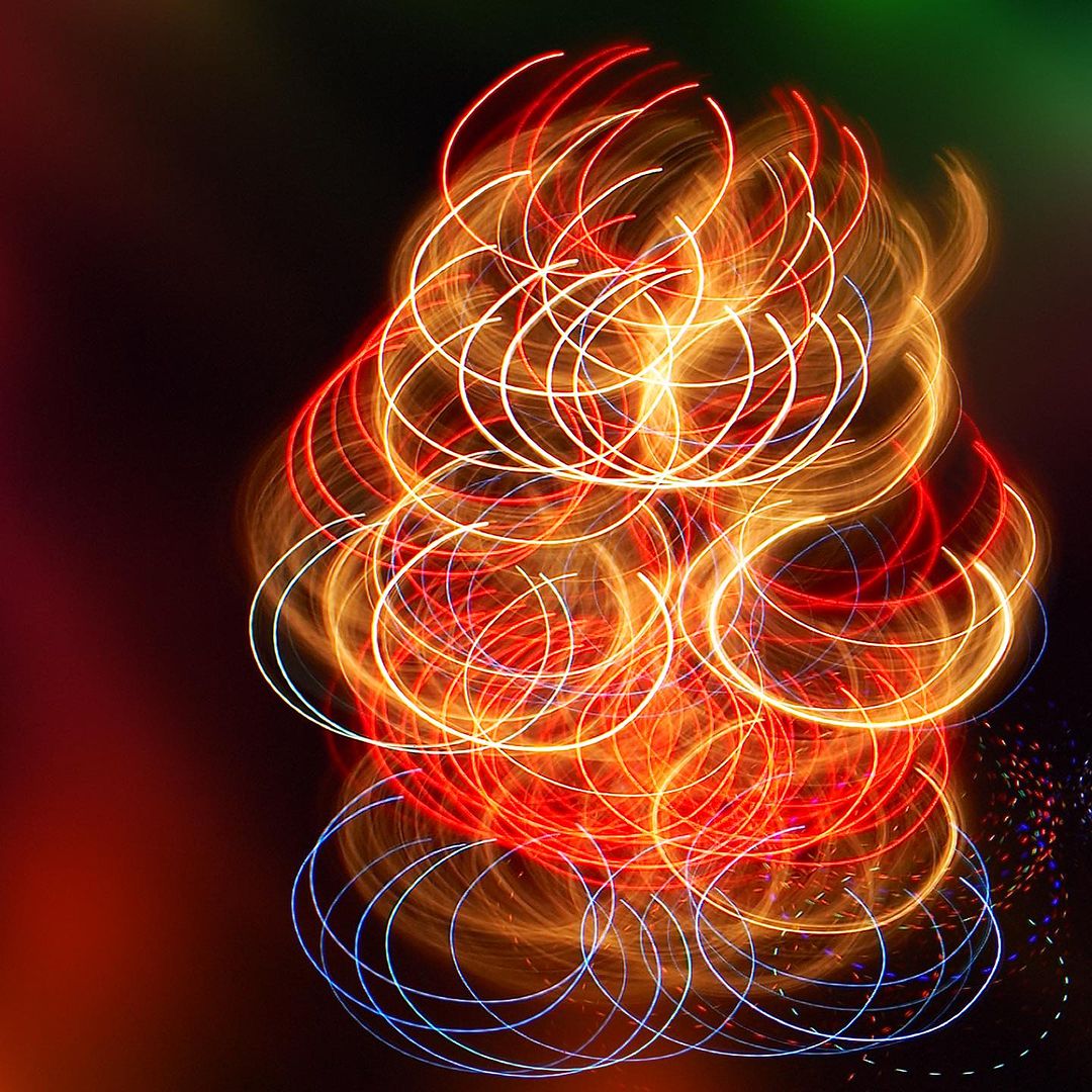 Abstract swirl of red, orange, and white light trails against a dark background, created with long exposure photography.