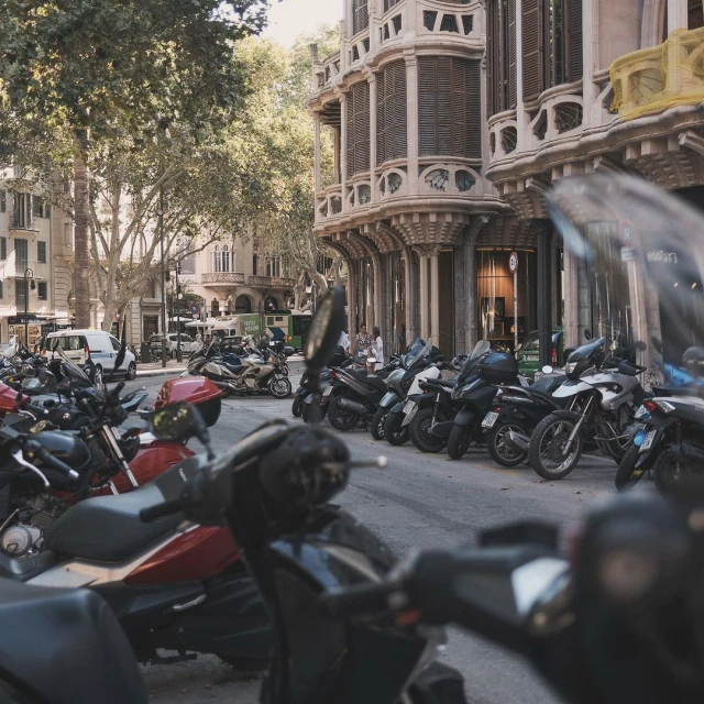 Cityscape featuring a row of parked motorcycles, with a background of historic buildings and lush trees under daylight conditions.