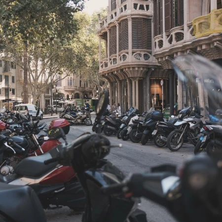 Cityscape featuring a row of parked motorcycles, with a background of historic buildings and lush trees under daylight conditions.