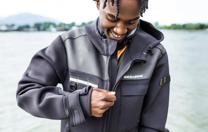 Young Black man zipping up a black neoprene Sea-Doo jacket outdoors near water by photographer Noel Hendrickson