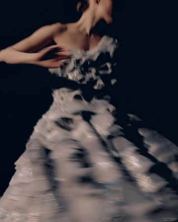 Motion blurred portrait of a woman wearing a white strapless dress with dark patterns against a black background.