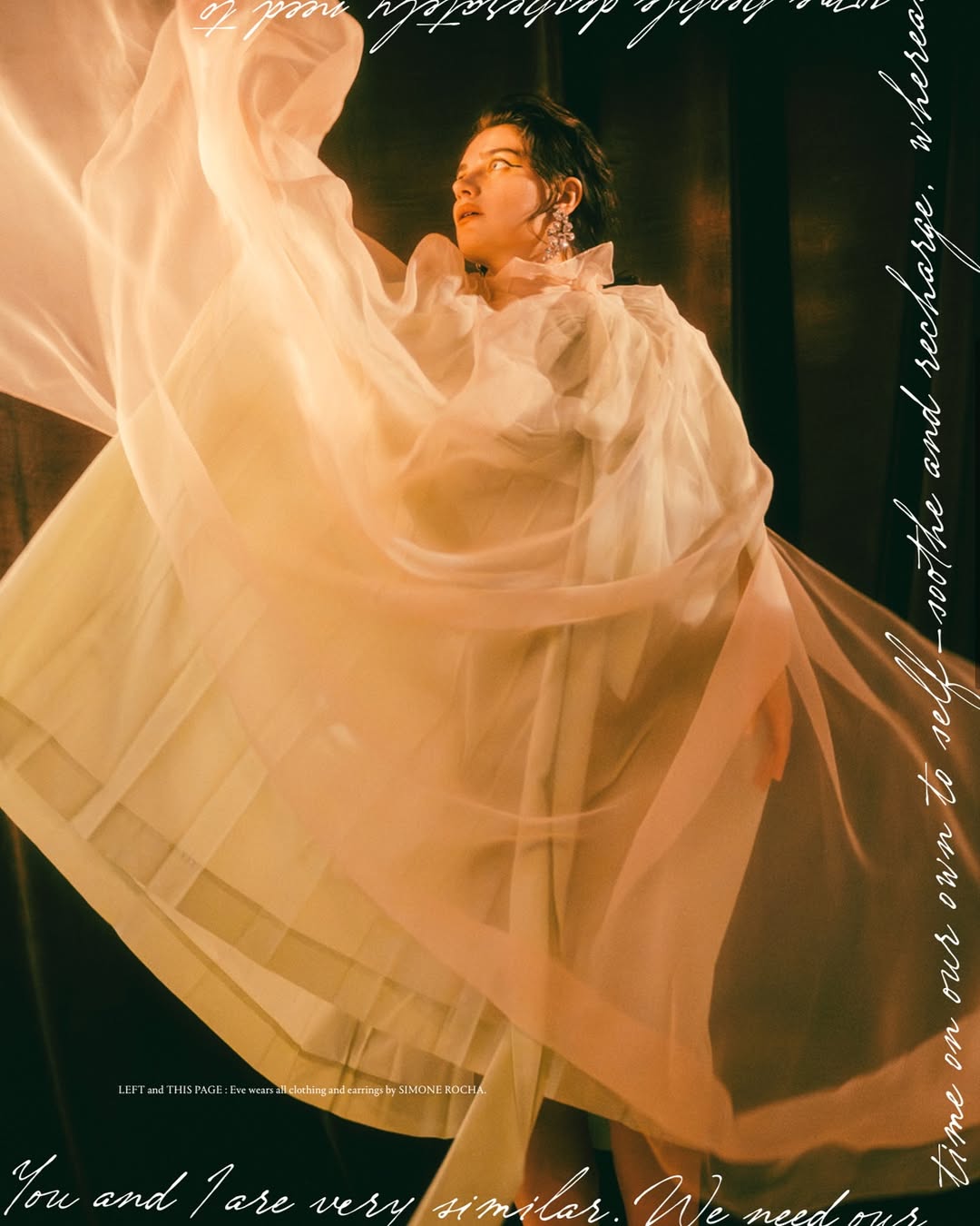 Woman in elegant white dress with sheer fabric, captured in a portrait with soft lighting and dark background for fashion editorial.