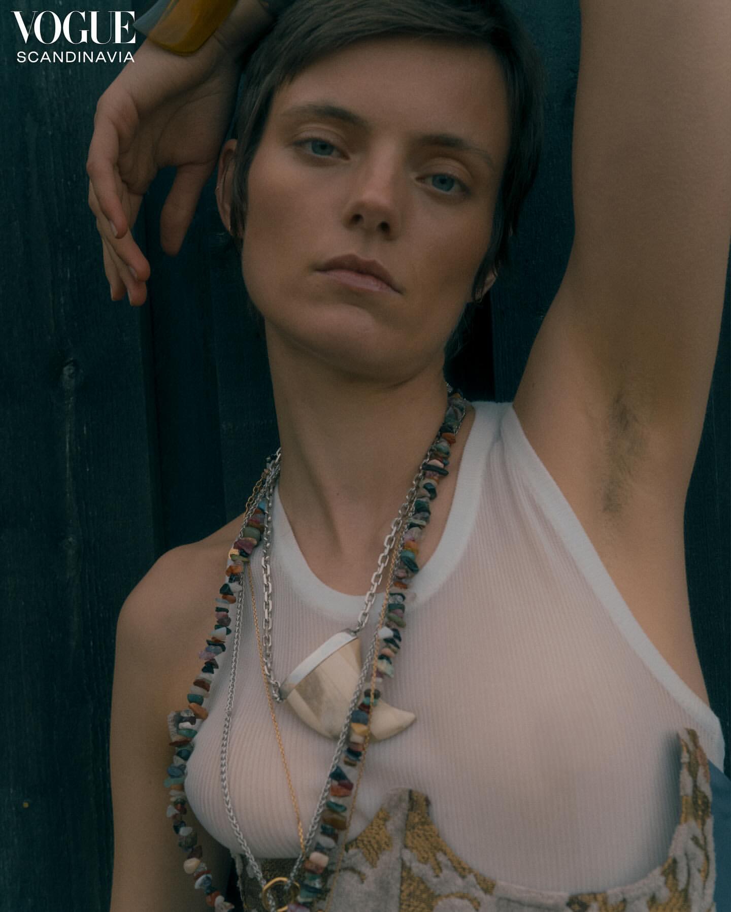 Close-up portrait of a model in a white tank top and layered necklaces against a dark wood background by Noemi Ottilia Szabo