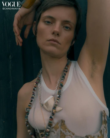 Close-up portrait of a model in a white tank top and layered necklaces against a dark wood background by Noemi Ottilia Szabo