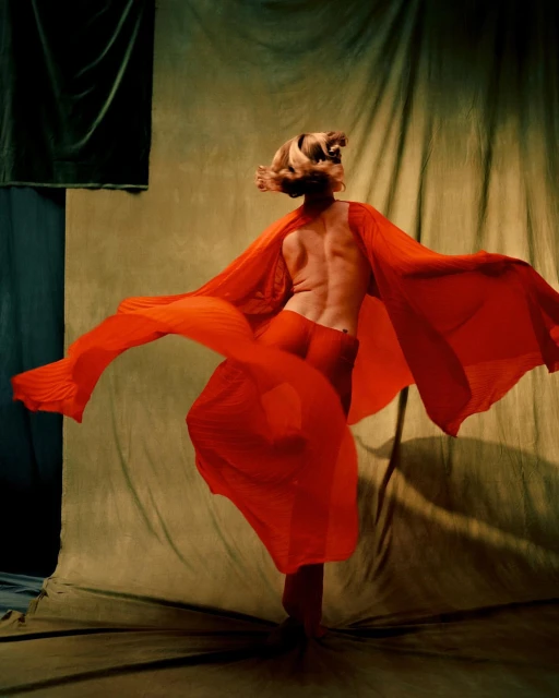 Back view of adult woman in red dress dancing expressively in studio setting with draped fabric background and dramatic lighting.