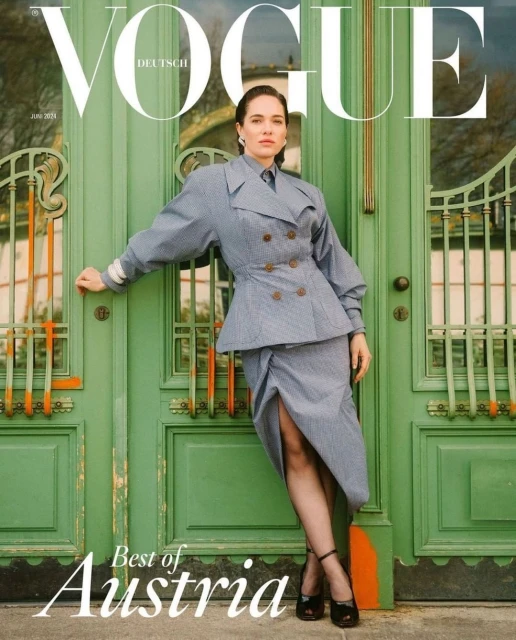 Vogue magazine cover featuring a woman in a grey suit posing against a green door with windows and the magazine title in white text.