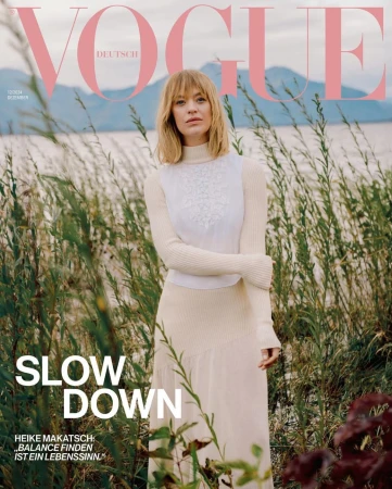 Heike Makatsch on the cover of Vogue Deutsch wearing a cream turtleneck sweater standing among tall grass by a lake.