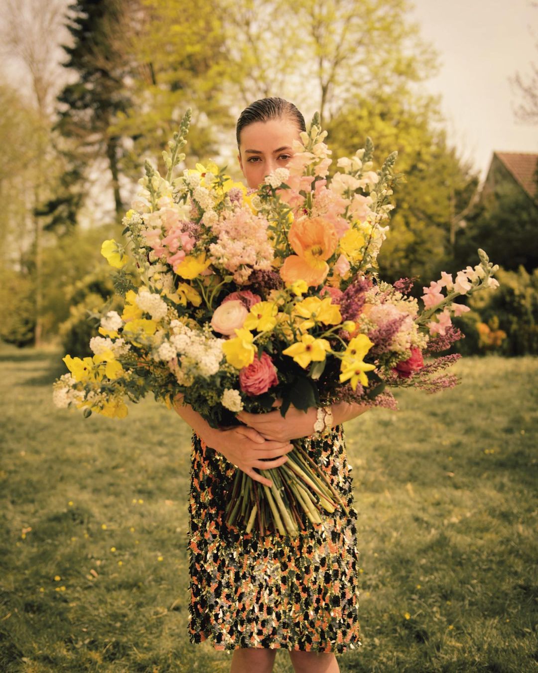 Woman holding a large colourful floral bouquet hiding her face outdoors in Paris by Noemi Ottilia Szabo