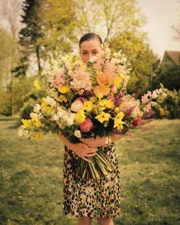 Woman holding a large colourful floral bouquet hiding her face outdoors in Paris by Noemi Ottilia Szabo